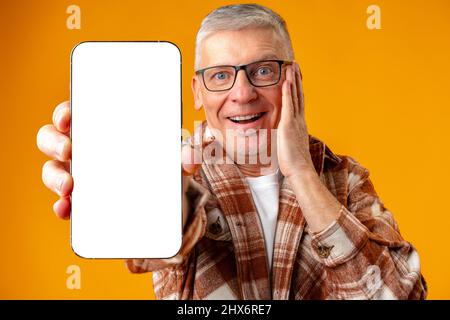 Photo de l'homme surprise senior pointe le doigt sur le smartphone sur fond jaune Banque D'Images