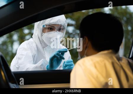 Médecin en PPE suit coronavirus test (covid-19) à homme en voiture par écouvillon nasal coton, drive test rapide Banque D'Images