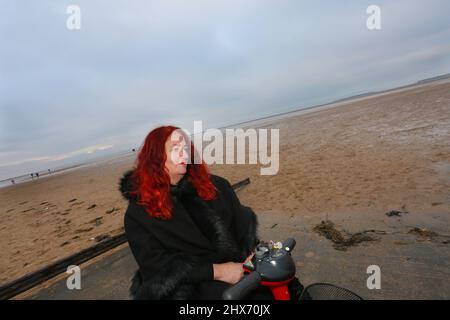 Les femmes avec les cheveux rouges à cheval un scooter de mobilité à la plage Banque D'Images