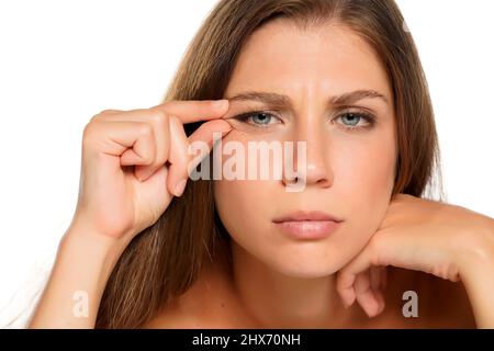 une jeune belle femme nerveuse avec des yeux bleus pinçant ses rides autour de ses yeux sur un fond blanc Banque D'Images