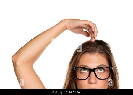 Demi portrait d'une jeune femme perplexe avec des lunettes de vue égratigne sa tête sur fond blanc Banque D'Images