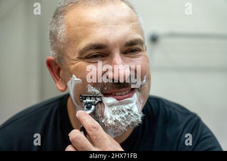 Un homme d'âge moyen qui se rasse sa barbe dans la salle de bains Banque D'Images