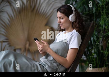 Jeune heureuse femme détendue dans un casque sans fil écoutant de la musique sur un smartphone dans le jardin à la maison Banque D'Images