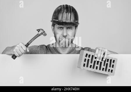 bricklayer. homme mature en casque avec marteau et brique. ouvrier barbu de constructeur Banque D'Images