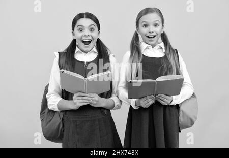 Surpris les enfants dans les uniformes formels lire les livres scolaires fond jaune, bibliothèque Banque D'Images