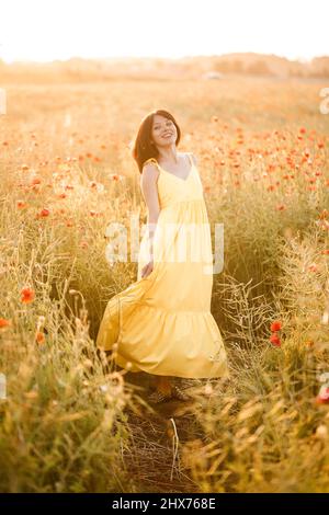 Belle jeune femme vêtue d'une robe jaune marchant dans un champ de pavot un jour d'été. Fille appréciant des fleurs dans la campagne. Mise au point sélective Banque D'Images