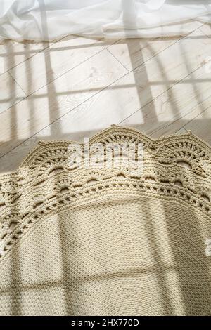 Tapis maison tricoté en fils épais, fait à la main: Un tapis fait à la main en fils beige se trouve sur le sol, le soleil brille dessus Banque D'Images
