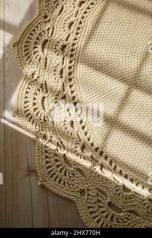 Tapis maison tricoté en fils épais, fait à la main: Un tapis fait à la main en fils beige se trouve sur le sol, le soleil brille dessus Banque D'Images
