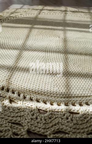Tapis maison tricoté en fils épais, fait à la main: Un tapis fait à la main en fils beige se trouve sur le sol, le soleil brille dessus Banque D'Images