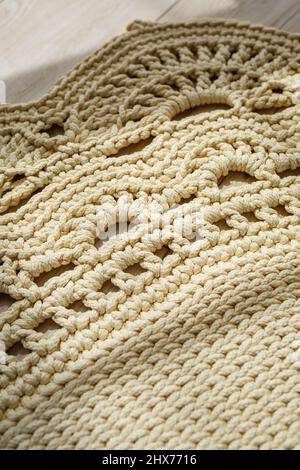 Tapis maison tricoté en fils épais, fait à la main: Un tapis fait à la main en fils beige se trouve sur le sol, le soleil brille dessus Banque D'Images