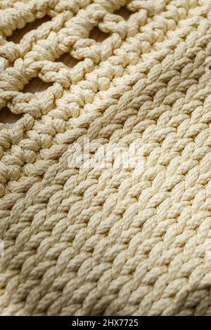 Tapis maison tricoté en fils épais, fait à la main: Un tapis fait à la main en fils beige se trouve sur le sol, le soleil brille dessus Banque D'Images