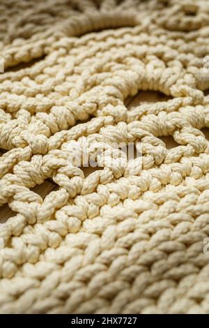 Tapis maison tricoté en fils épais, fait à la main: Un tapis fait à la main en fils beige se trouve sur le sol, le soleil brille dessus Banque D'Images