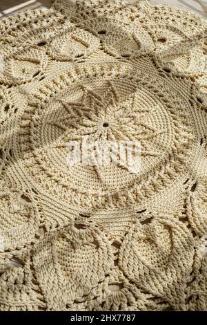 Tapis maison tricoté en fils épais, fait à la main: Un tapis fait à la main en fils beige se trouve sur le sol, le soleil brille dessus Banque D'Images
