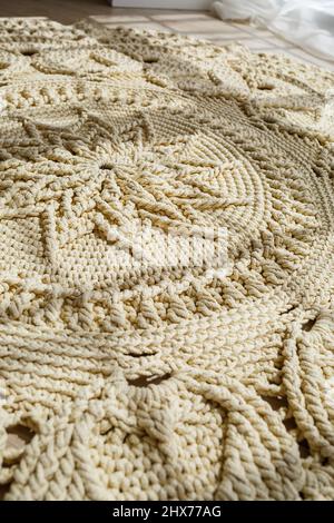 Tapis maison tricoté en fils épais, fait à la main: Un tapis fait à la main en fils beige se trouve sur le sol, le soleil brille dessus Banque D'Images