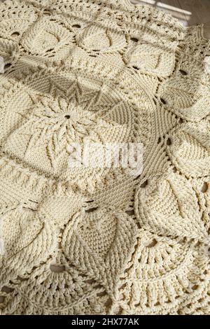 Tapis maison tricoté en fils épais, fait à la main: Un tapis fait à la main en fils beige se trouve sur le sol, le soleil brille dessus Banque D'Images