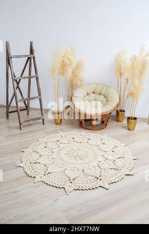 Tapis fait maison en fils épais, fait à la main: Un tapis fait à la main en fils beige se trouve dans le salon près du fauteuil, l'art de Knitt Banque D'Images