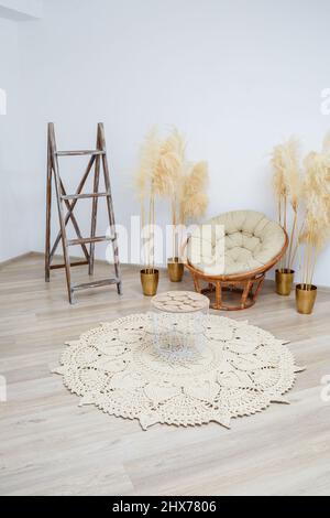 Tapis fait maison en fils épais, fait à la main: Un tapis fait à la main en fils beige se trouve dans le salon près du fauteuil, l'art de Knitt Banque D'Images