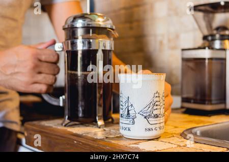 gros plan d'un adulte méconnaissable tenant une tasse de café et une cafetière avec ses mains, sur le comptoir, préparant le café pour le petit déjeuner à la maison. Banque D'Images