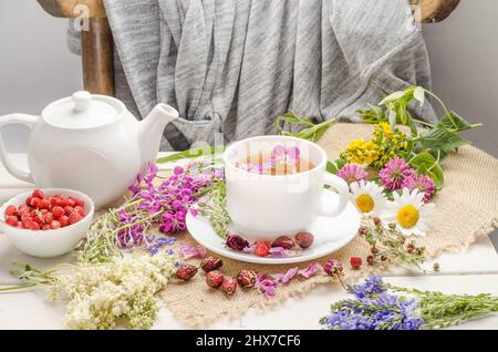 Tisane au rosehip, camomille et trèfle dans une tasse blanche sur une table blanche en bois avec des fleurs. Banque D'Images