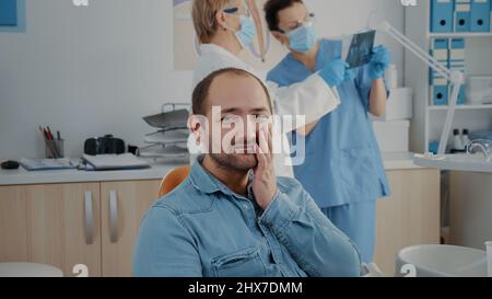 Portrait d'un patient avec mal de dents regardant la caméra dans le bureau de la dentisterie. Homme dans la douleur ayant un rendez-vous stomatologique pour faire la procédure d'extraction, se sentant blessé en raison de problèmes de caries. Banque D'Images