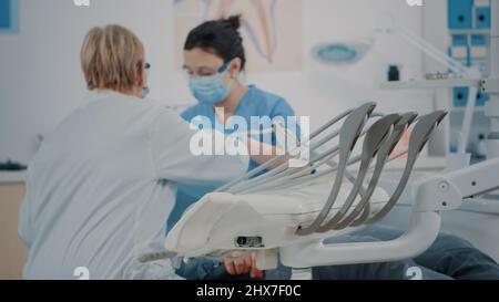 Équipe de dentisterie examinant le patient dans l'armoire de stomatologie, en utilisant des outils dentaires pour traiter les problèmes de prothèse dentaire. Infirmière et dentiste consultant homme, faisant la procédure stomatologique à la visite de contrôle. Banque D'Images