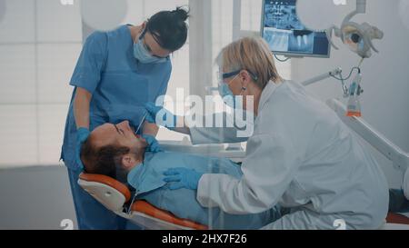 Équipe de dentisterie qui fait la consultation des dents pour traiter le patient avec des maux de dents, en utilisant l'équipement dentaire dans le bureau de stomatologie. Dentiste et assistant examinant la prothèse après la procédure de forage. Banque D'Images