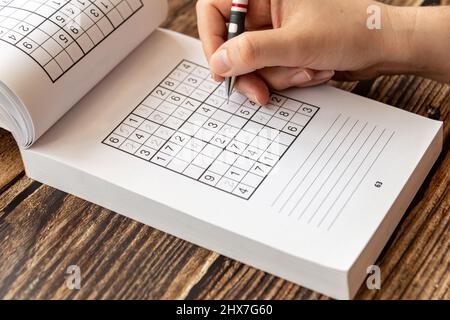 Personne résolvant un puzzle de sudoku sur une table en bois. Banque D'Images