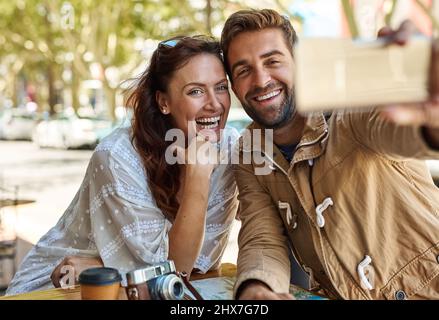 Devinez où nous sommes. Photo d'un couple touristique heureux prenant un selfie tout en se relaxant dans un café-terrasse ensemble. Banque D'Images