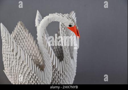 Une paire de cygnes origami sur fond gris. Deux oiseaux assemblés à partir de morceaux de papier triangulaires blancs. Un symbole de famille, d'amour, de loyauté et de Banque D'Images
