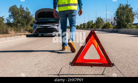 Voiture avec des problèmes et l'homme a mis un triangle rouge pour avertir les autres usagers de la route. Homme conducteur debout près d'une voiture brisée avec capot ouvert, en attente d'aide. Banque D'Images