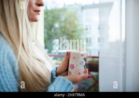 Vue rapprochée d'une femme blonde qui regarde à l'extérieur par une fenêtre. Banque D'Images