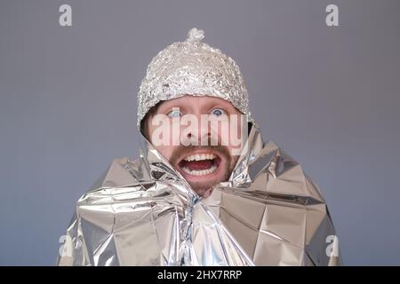 Jeune homme dans un chapeau de feuille d'aluminium étant peur et stressé. Banque D'Images