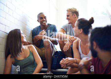 Il sait faire rire le groupe. Plan court d'étudiants de l'université parlant en s'asseyant sur les marches d'un escalier. Banque D'Images