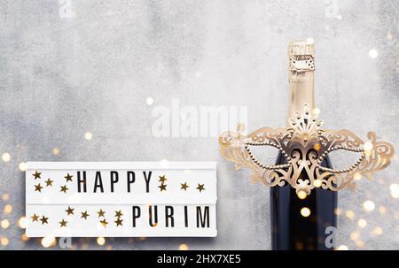Happy Purim écrit en visionneuse, champagne et masque de carnaval doré sur fond gris. Concept de fête du carnaval de Purim. Vue de dessus Banque D'Images