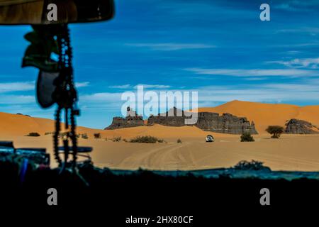 Vue sur le pare-brise depuis l'intérieur d'une voiture de dunes de sable, montagnes rocheuses du désert mesa après un véhicule tout-terrain 4X4. Herbes sèches et arbres, ciel bleu. Banque D'Images