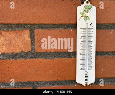 un thermomètre à colonne blanc avec une échelle celsius est accroché sur un mur de briques rouges Banque D'Images