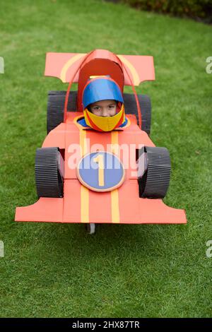 Enfants portant des modèles/costumes de voitures de course en carton, jouant dans le jardin Banque D'Images