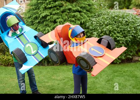 Enfants portant des modèles/costumes de voitures de course en carton, jouant dans le jardin Banque D'Images