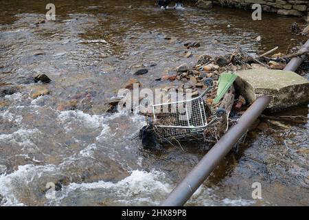 Chariot à provisions plastique et autres débris dans la rivière piégés derrière un tuyau métallique traversant la rivière Banque D'Images