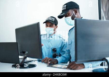 Le meilleur détail de sécurité pour votre entreprise. Photo de deux jeunes gardes de sécurité masqués en service à la réception d'un bureau. Banque D'Images