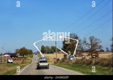 Deux hommes de ligne se trouvent dans des cueilleurs de cerises qui travaillent sur des lignes téléphoniques dans les zones rurales de l'Arkansas. La voiture a ralenti pour contourner l'équipement. Banque D'Images