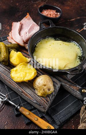 La raclette suisse a fondu le fromage avec de la pomme de terre bouillie et du jambon sur bois.Arrière-plan sombre.Vue de dessus Banque D'Images