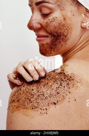 Faites ce que vous devez faire pour que votre peau reste lisse. Photo courte d'une jeune femme attrayante souriant tout en appliquant un masque de café sur son corps à la maison. Banque D'Images