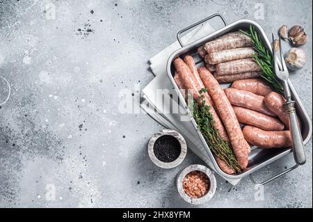 Assortiment de saucisses crues. Viande de bœuf, porc, agneau et poulet hachez les saucisses dans un plateau de cuisine en acier aux herbes. Arrière-plan gris. Vue de dessus. Copier l'espace Banque D'Images