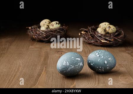 .Oeufs de poulet et de caille peints dans des nids sur une table en bois brun sur un fond sombre Banque D'Images