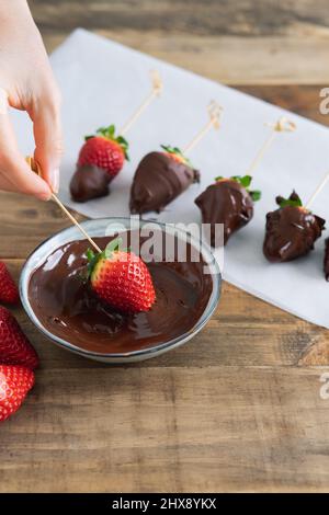 Fraises au chocolat sur fond de bois. Trempette à la main de fraise dans un bol de chocolat. Copier l'espace. Photo verticale. Banque D'Images