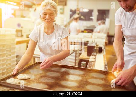 Une jeune femme en tant que boulangère en formation travaille dans la boulangerie et met des tresses de levure sur une plaque de cuisson Banque D'Images