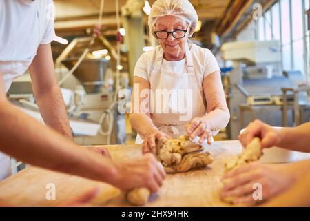 Boulanger femme senior avec expérience pétrir de la pâte avec des collègues dans une grande boulangerie Banque D'Images