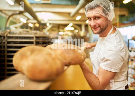 Jeune homme boulanger apprenti avec du pain cuit prêt sur une pelle à pain dans la boulangerie Banque D'Images