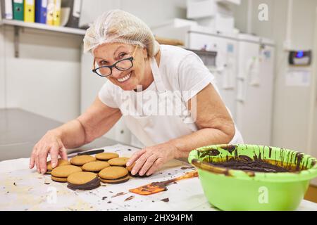 Femme senior boulangère avec expérience décorent des biscuits doubles avec du chocolat dans une boulangerie Banque D'Images